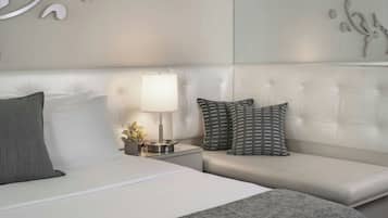 A modern hotel room with a white bed, grey and patterned pillows, a bedside table with a lamp, and decorative wall art.