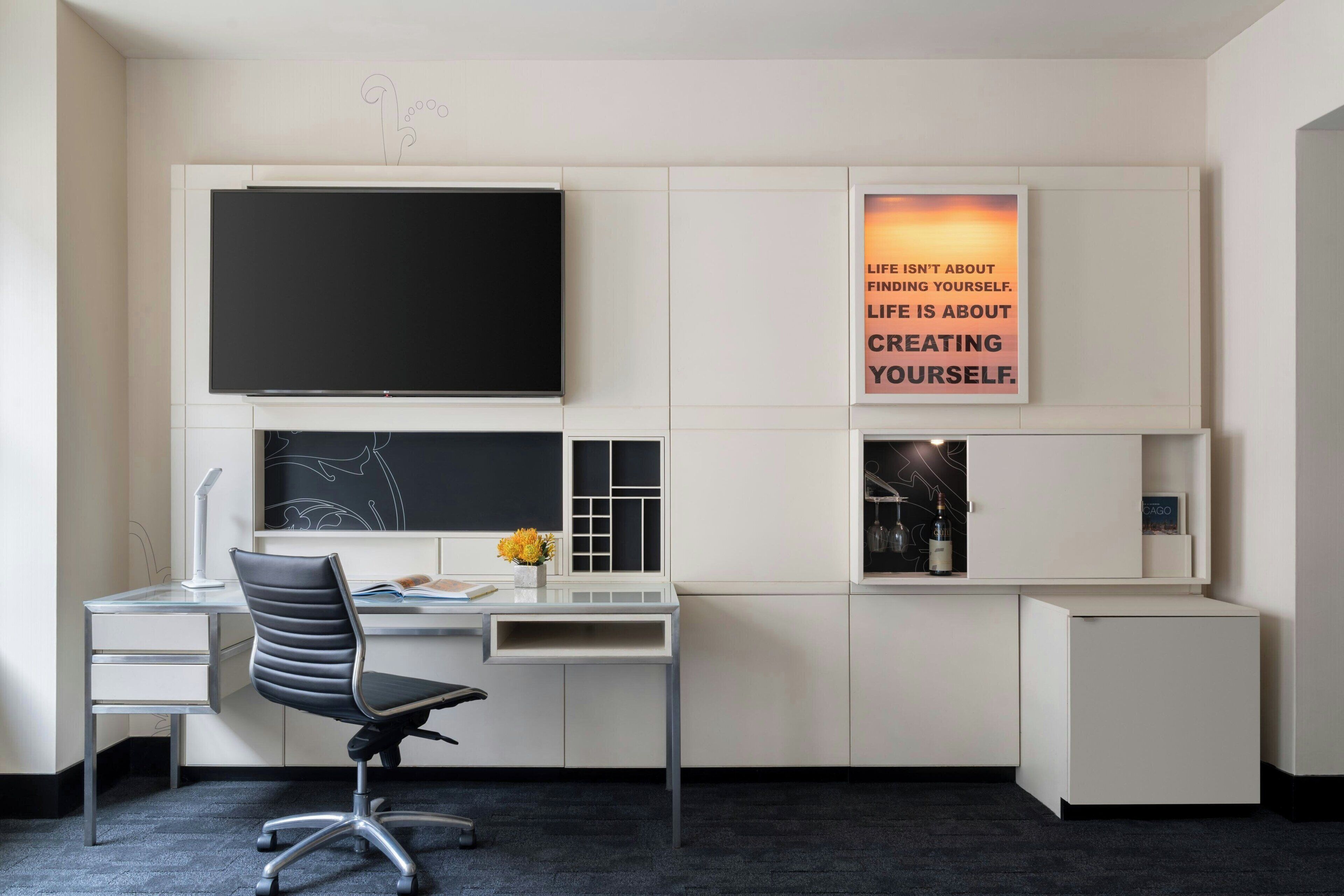 A modern office desk with a flat-screen TV, a computer, and a chair.