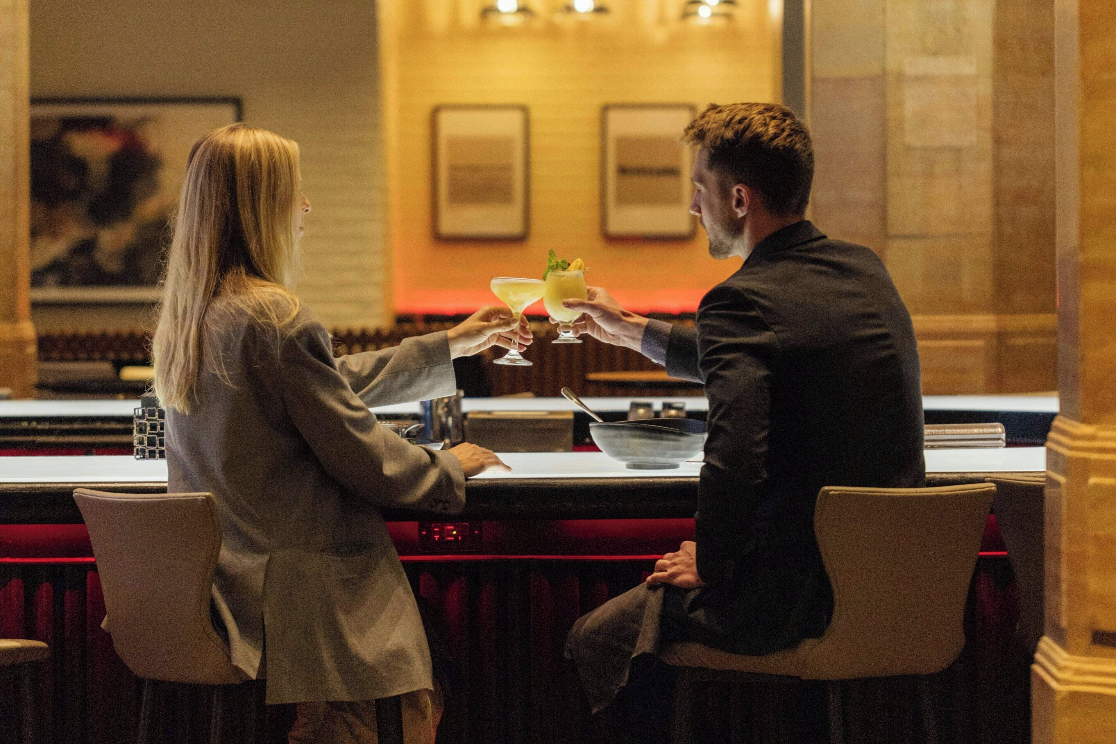 A man and a woman at a bar in a hotel, holding drinks.