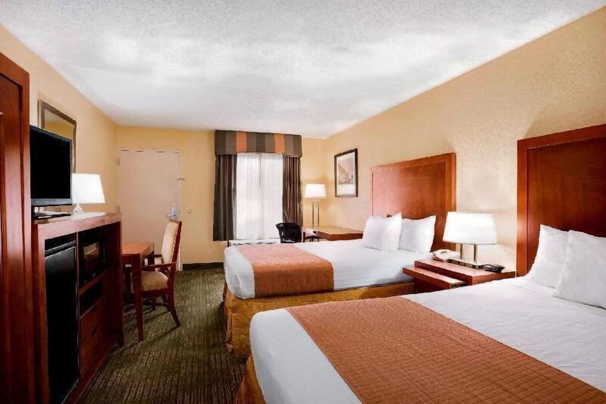 A hotel room with two beds, a desk, a chair, a television, and a window with curtains.