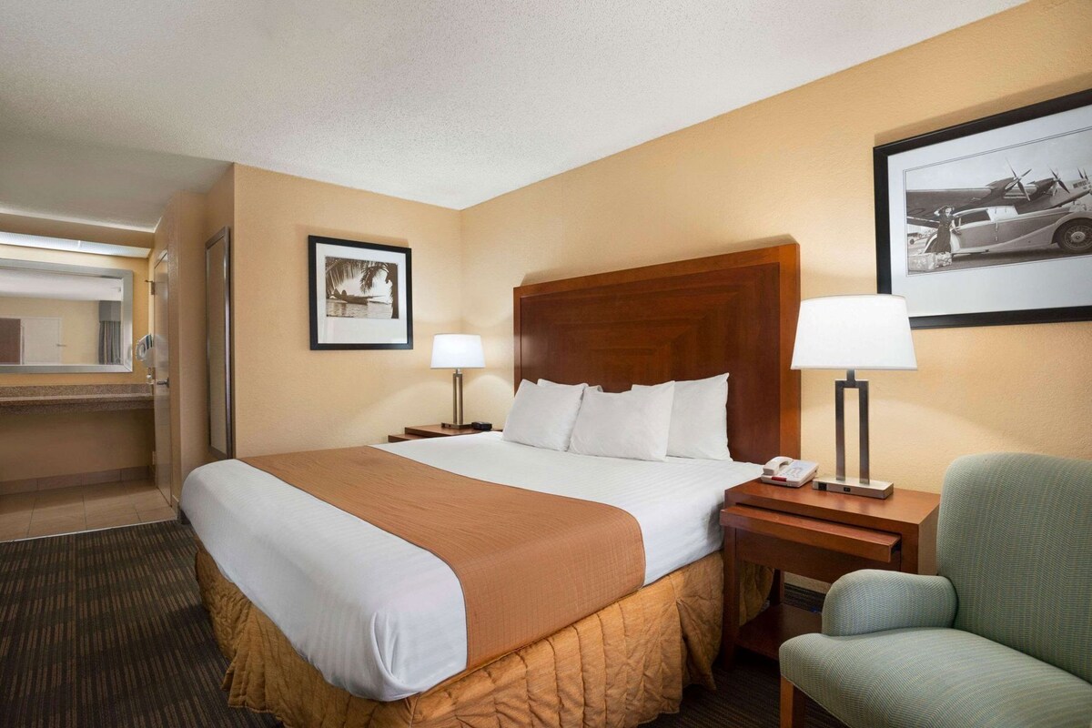 A hotel room with a bed, two bedside tables, a chair, a framed picture, and a lamp.
