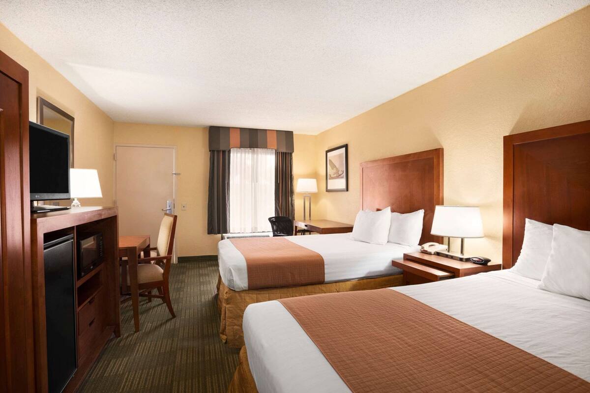 A hotel room with two beds, a desk with a TV, a chair, a desk lamp, and a framed picture on the wall.