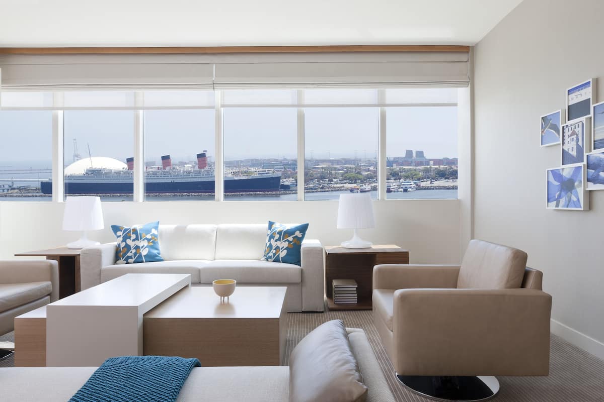A modern hotel room with a large window offering a view of a ship and cityscape.