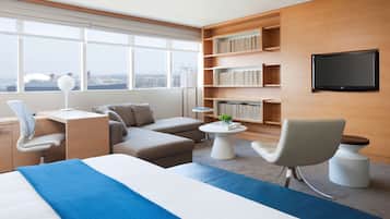 Une chambre d’hôtel moderne, dotée d’un grand lit, d’un bureau, d’un canapé, d’un téléviseur fixé au mur et d’une bibliothèque.