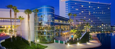 A modern hotel with a glass facade, a pool area, and palm trees.