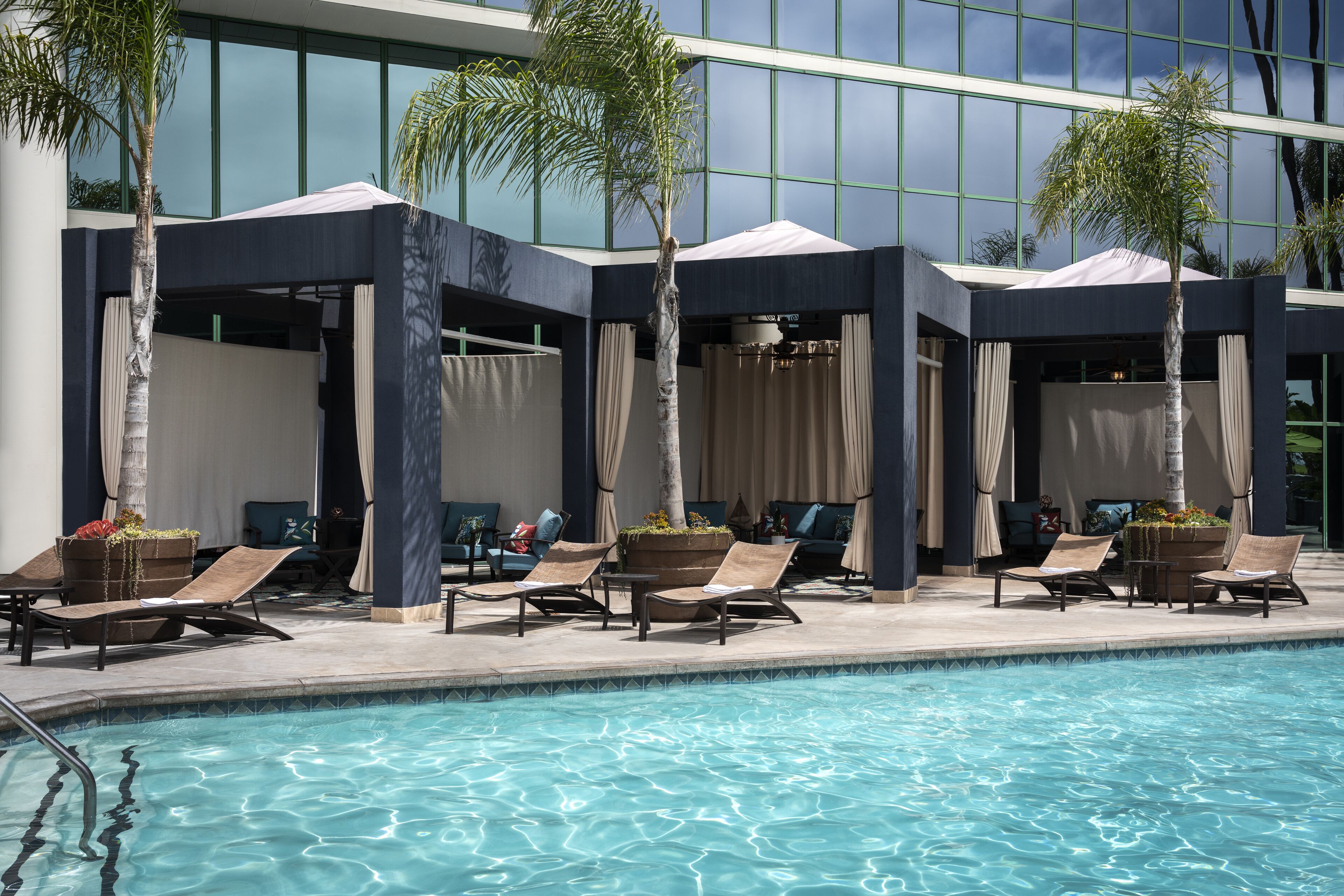 A pool area with lounge chairs and umbrellas, surrounded by a modern building with large windows.