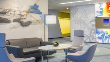 Ein stilvoller Lounge-Bereich mit grauem Sofa, zwei blauen Sessel, einem kleinen runden Tisch mit Obstschale und abstrakter Wandkunst.