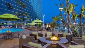 A poolside area with wicker furniture, green umbrellas, and a fire pit. - Hyatt Regency Long Beach (Long Beach)