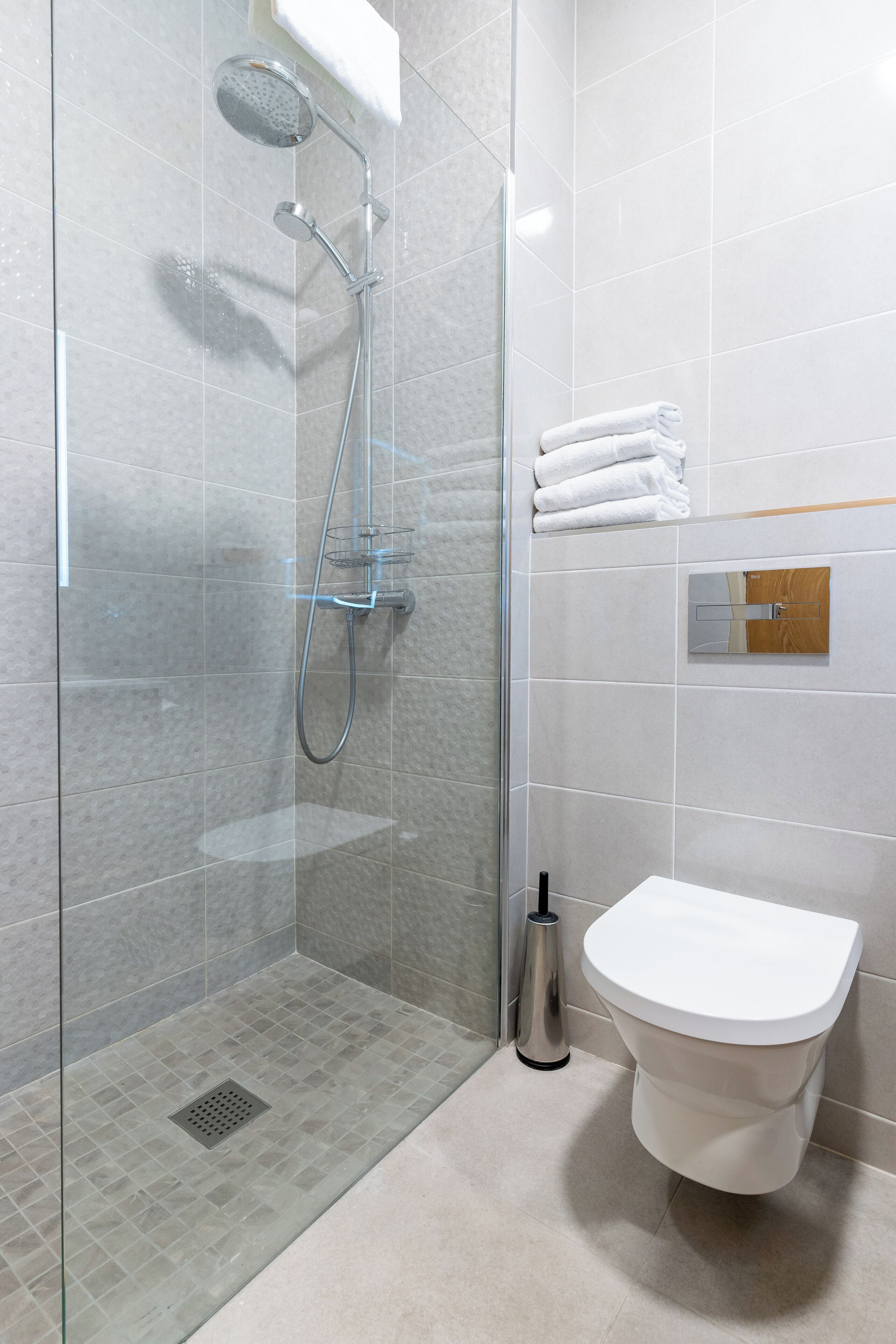 A modern bathroom with a glass-enclosed shower, a white toilet, and neatly stacked towels.