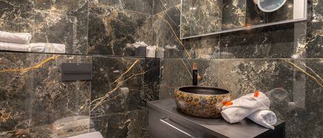 Un baño moderno con salpicadero de mármol, un lavabo redondo de diseño original, inodoro y tocador con cajones.