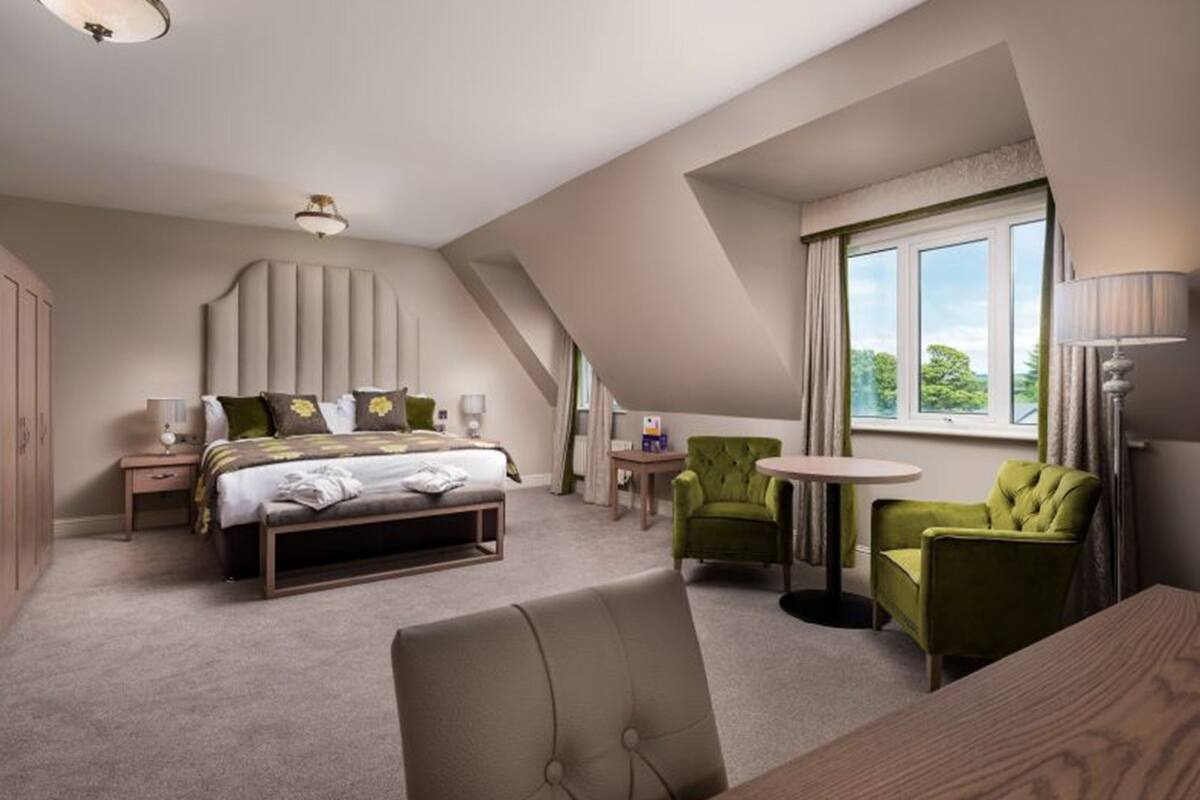 Une chambre à coucher avec un lit, deux fauteuils, une petite table et une fenêtre avec des rideaux.