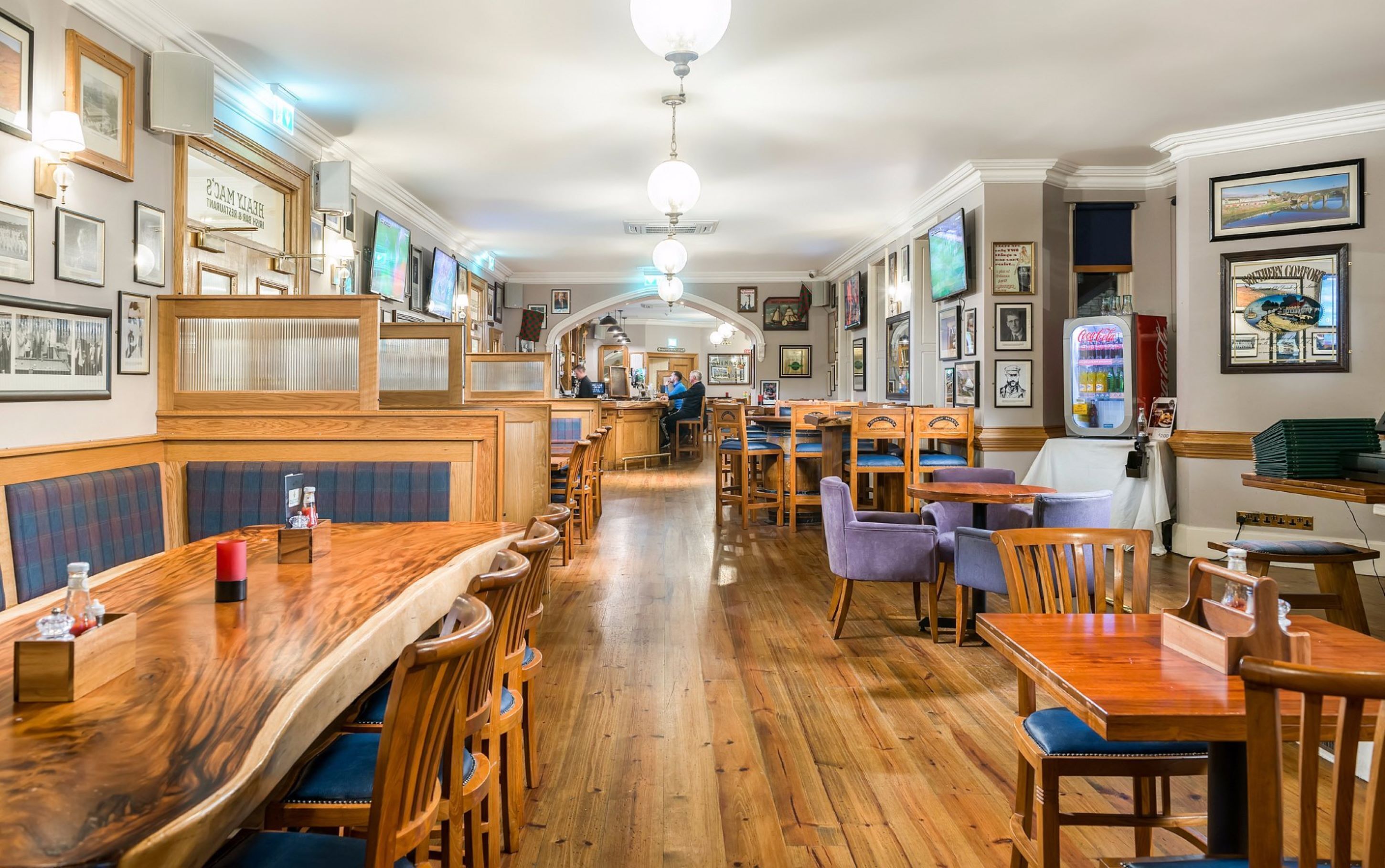 A restaurant with wooden booths, tables, and chairs. There are framed pictures on the walls and a Coca-Cola vending machine.