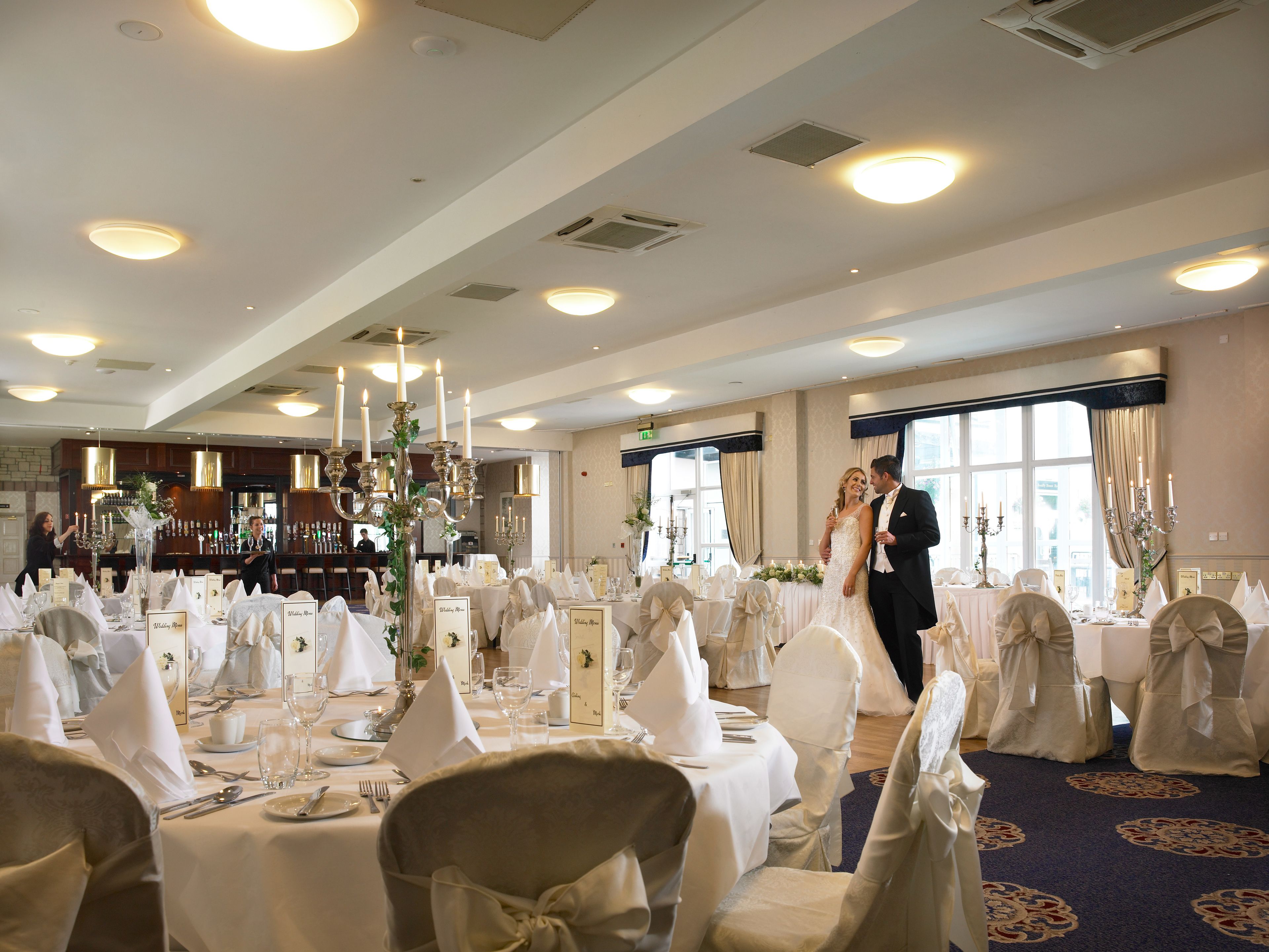A wedding reception with round tables, white tablecloths, and chairs with white sashes.
