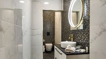 Un baño moderno con tocador de mármol, un espejo redondo y un inodoro visible al fondo.