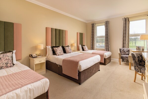 A hotel room with two beds, a desk, and a chair. There are curtains on the windows and a lamp on the desk.