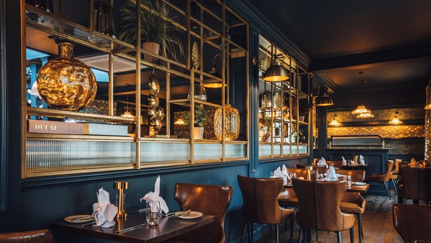 Een restaurantinterieur met houten tafels en stoelen, een groot raam met decoratieve objecten en hangende吊灯.