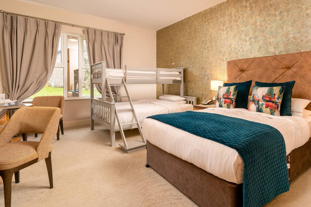 Une chambre d’hôtel avec un lit superposé, un bureau, une chaise et un grand lit avec une tête de lit.