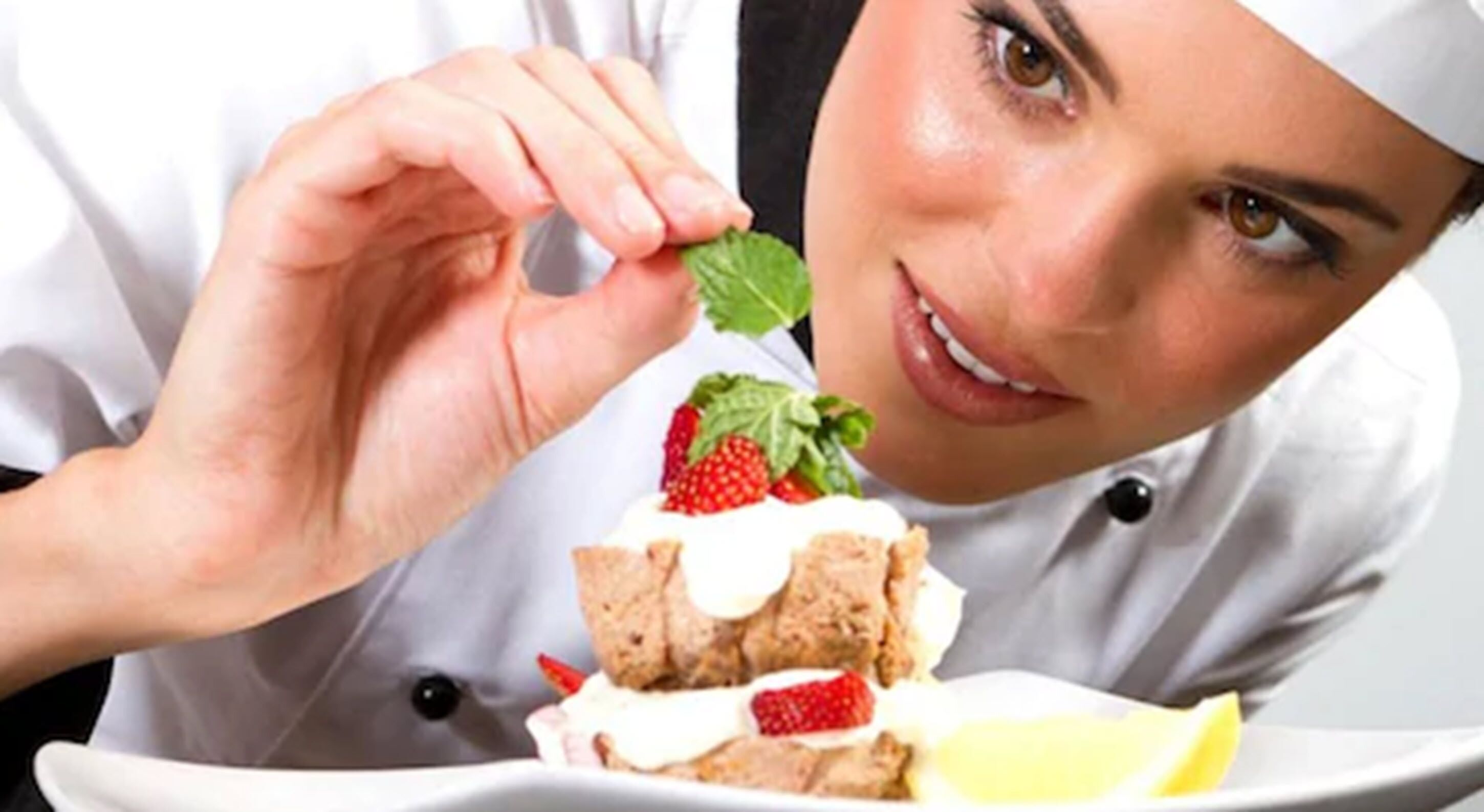 A person in a chef's uniform holding a piece of cake with strawberries and cream.