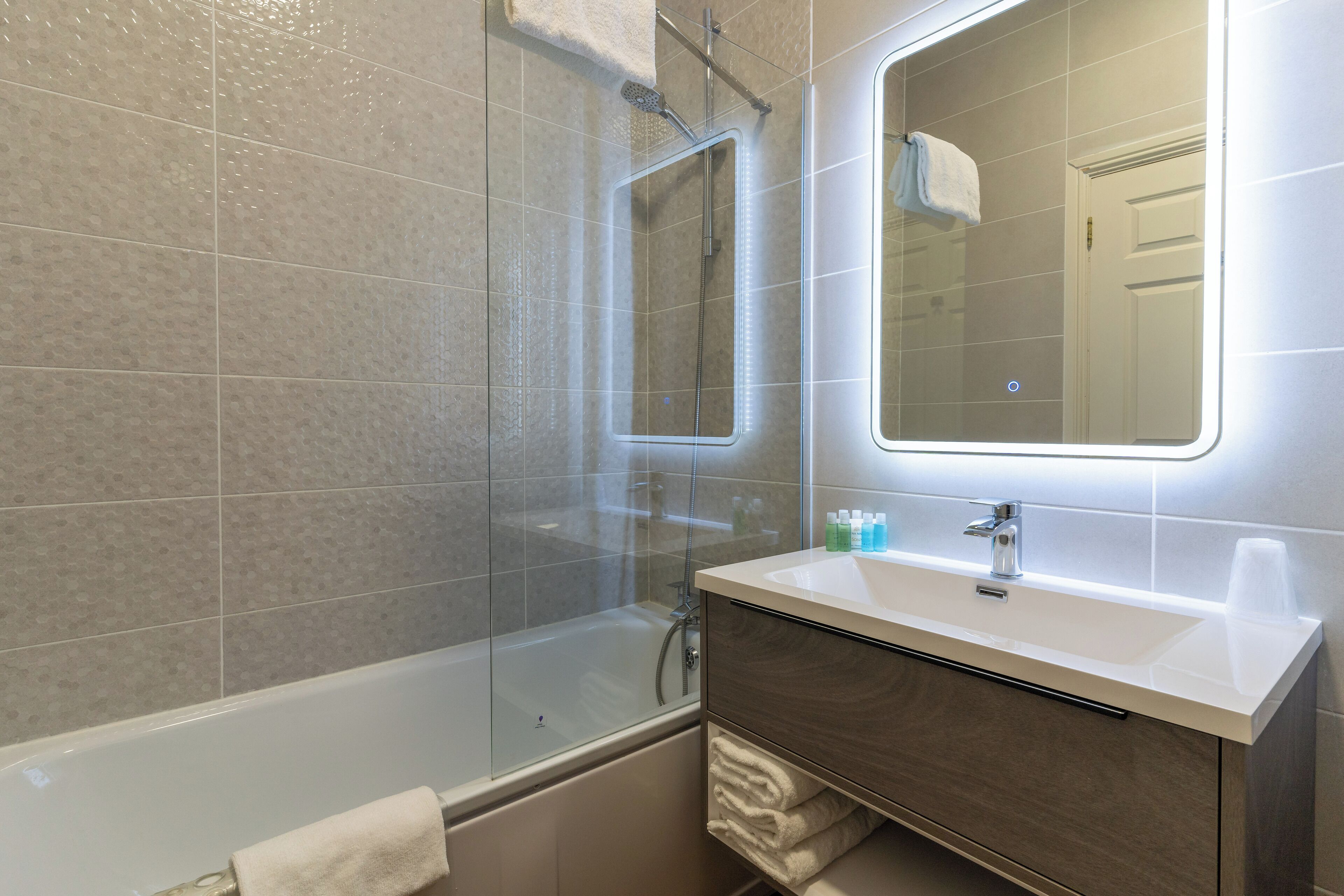 Un bagno moderno con doccia vetro, vasca, lavabo con specchio e porta asciugamani.