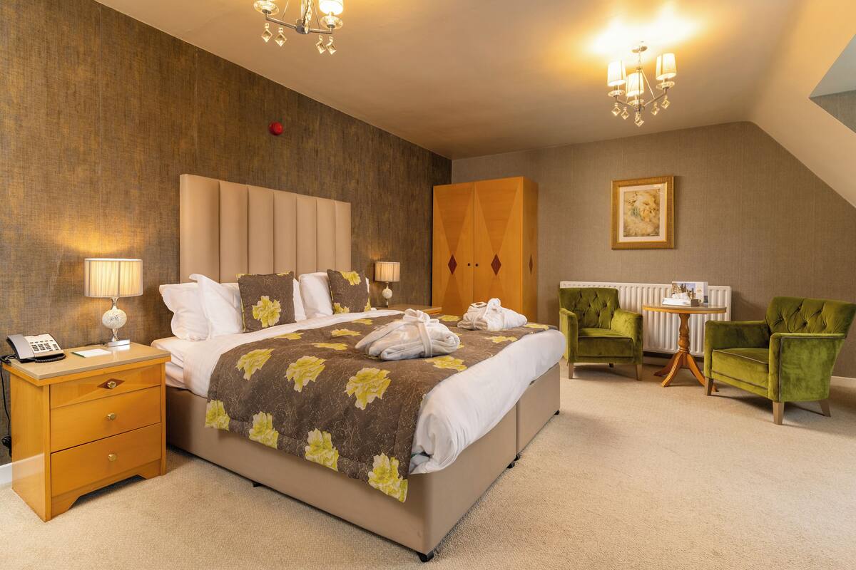 Une chambre d’hôtel avec un grand lit, des lampes de chevet, une table de chevet, un bureau, deux chaises et un radiateur.
