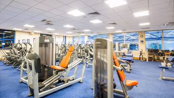 A gym with various exercise machines, a blue carpet, and a large window with a view of the sky.