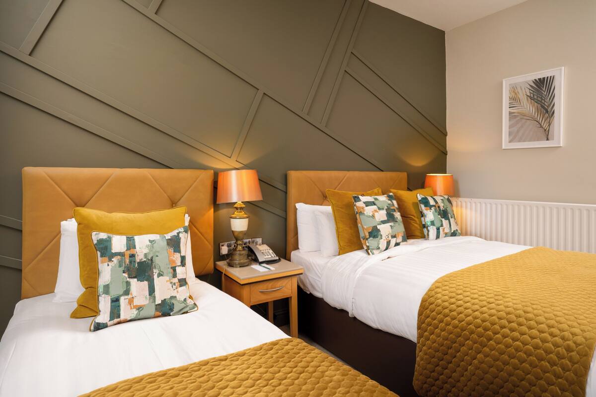 Une chambre d’hôtel avec deux lits, une table de chevet avec une lampe et un tableau encadré au mur.
