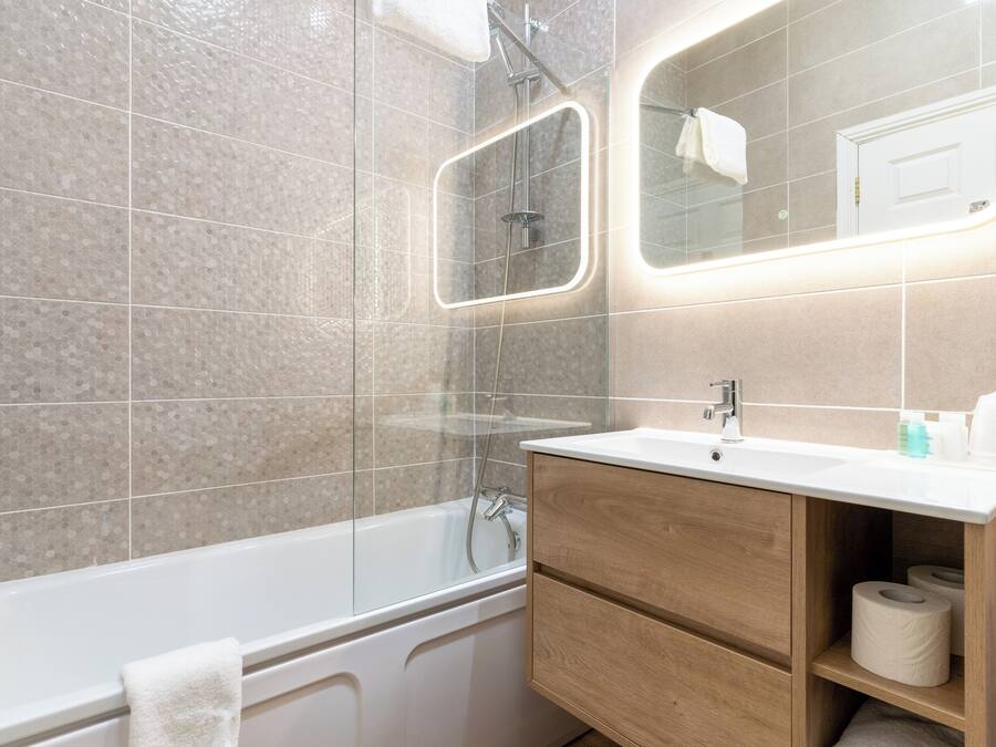 A modern bathroom with a glass-enclosed shower, a white bathtub, and a wooden vanity with a mirror.
