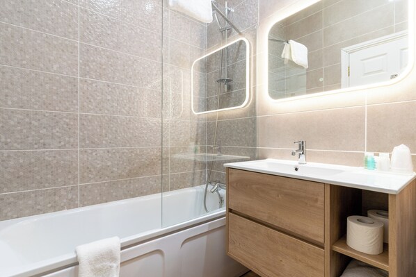 A modern bathroom with a glass-enclosed shower, a white bathtub, and a wooden vanity with a mirror.