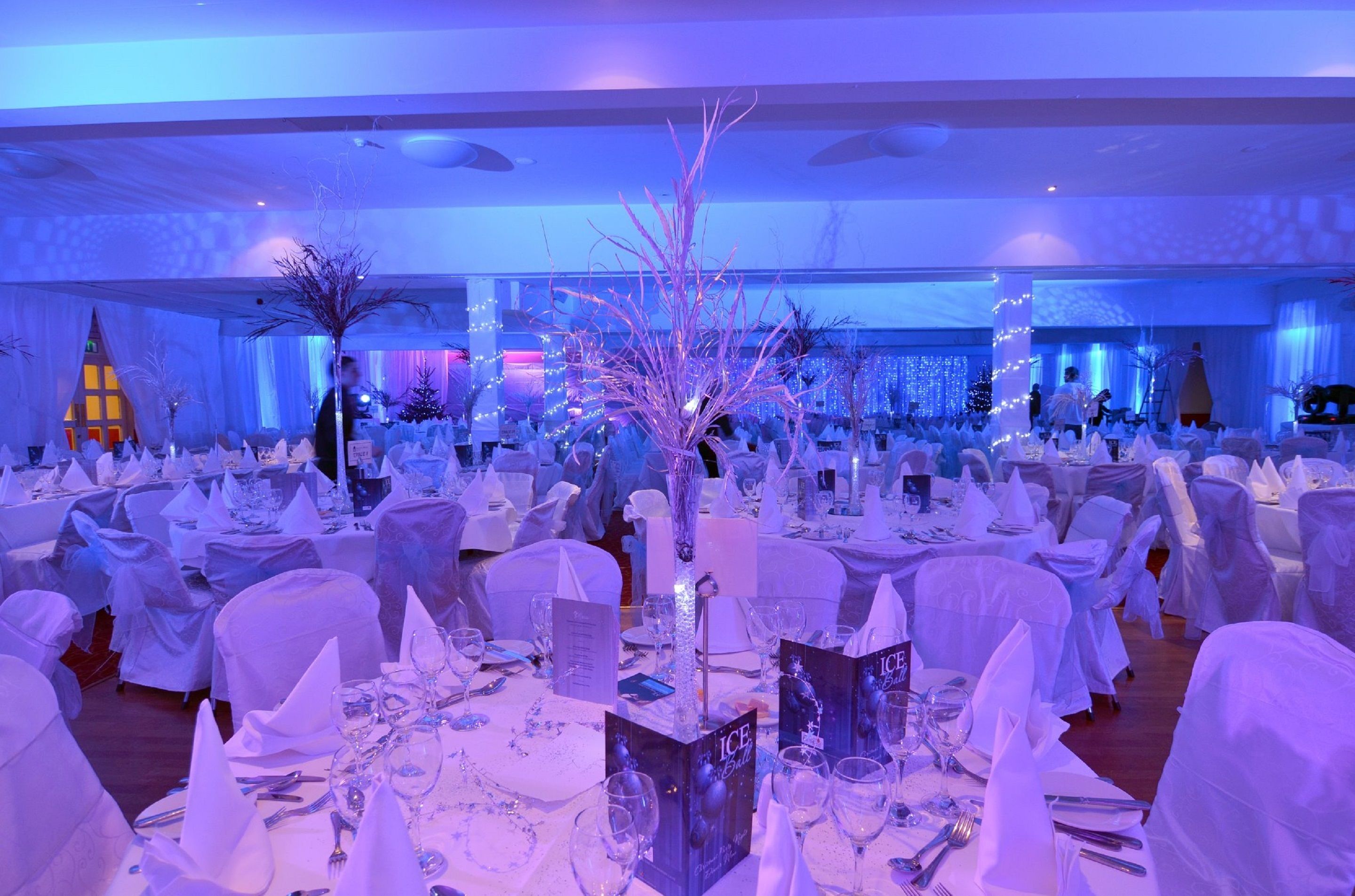 Un salón de banquetes con mesas redondas cubiertas con manteles blancos y sillas, dispuesto para un evento formal.