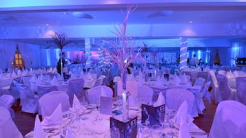 Un salón de banquetes con mesas redondas cubiertas con manteles blancos y sillas, dispuesto para un evento formal.