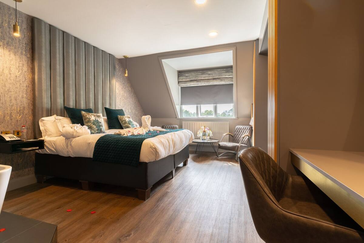 Une chambre moderne avec un grand lit, une petite table ronde, une chaise et une fenêtre donnant sur le ciel.