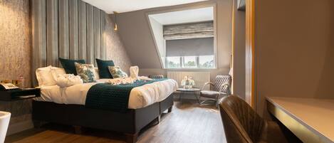 A modern bedroom with a large bed, a small round table, a chair, and a window with a view of the sky.
