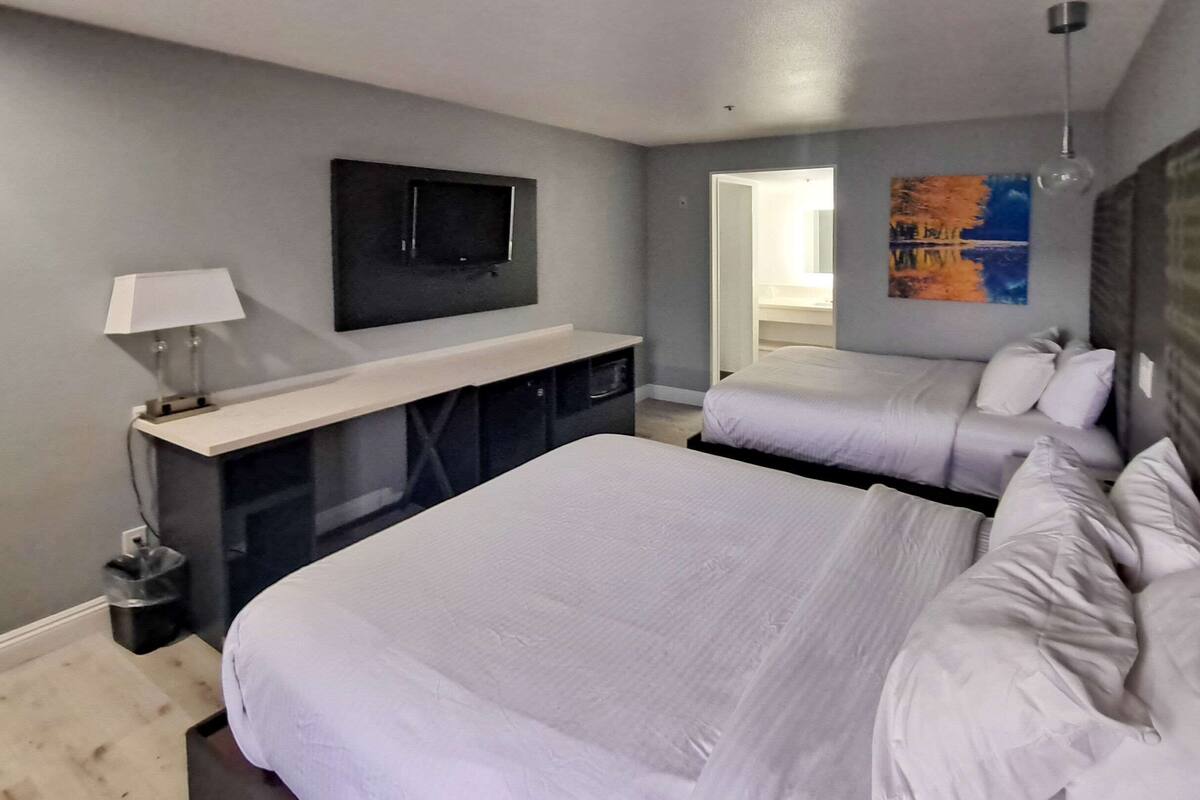 A hotel room with two beds, a TV mounted on the wall, a desk with a lamp, and a painting on the wall.