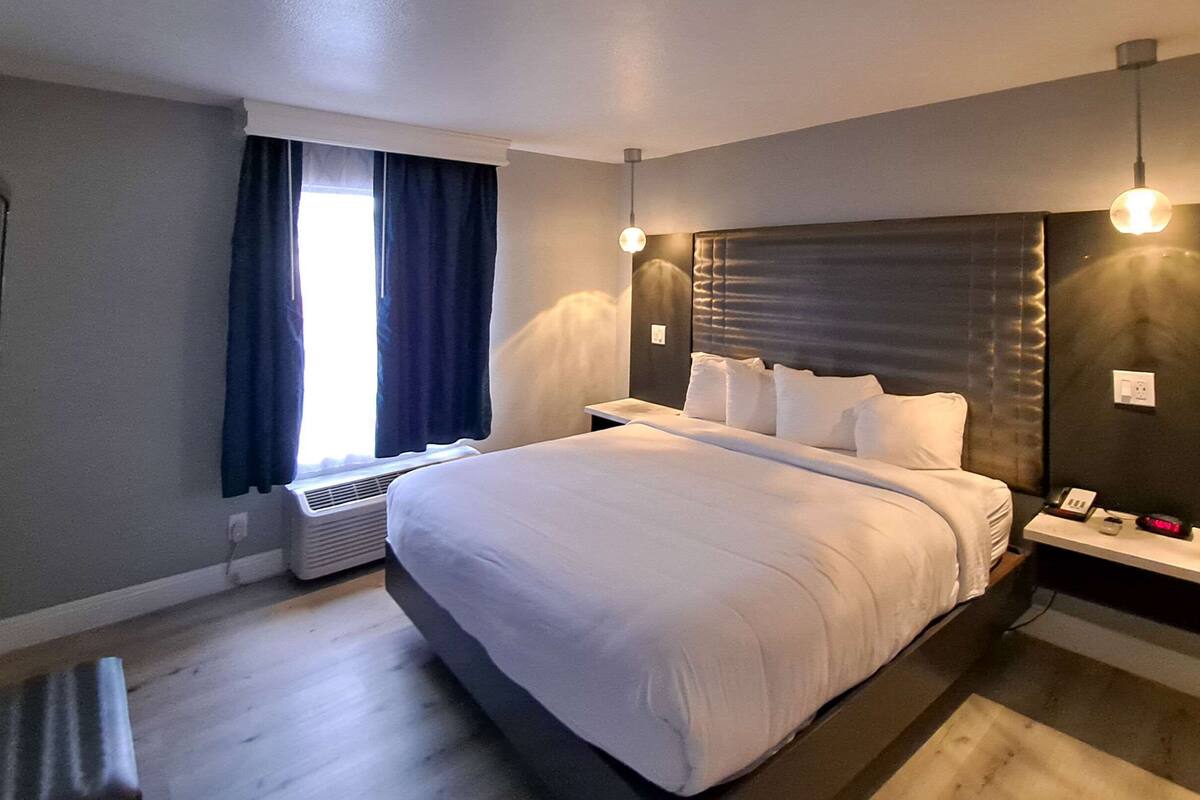 A modern hotel room with a large bed, bedside tables, a heater, and a window with curtains.