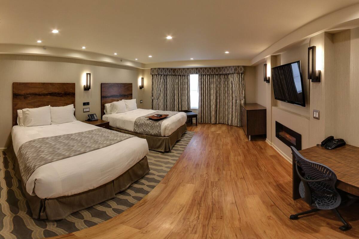 A hotel room with two beds, a desk, a chair, a TV, and a fireplace.