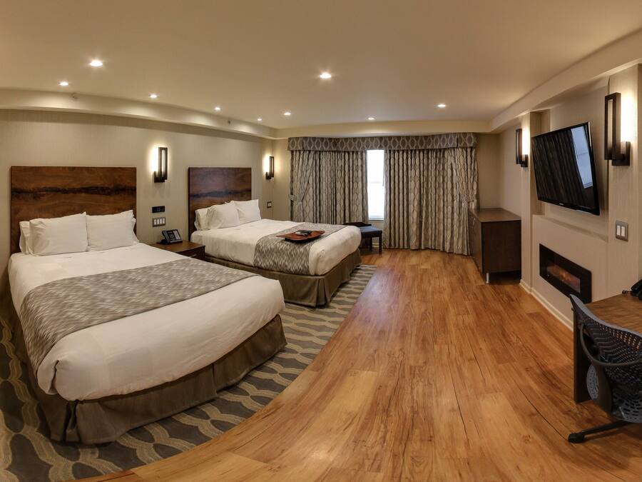 A hotel room with two beds, a desk, a chair, a TV, and a fireplace.