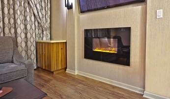 A living room with a wooden cabinet, a flat-screen TV mounted on the wall, and a fireplace with a visible fire.