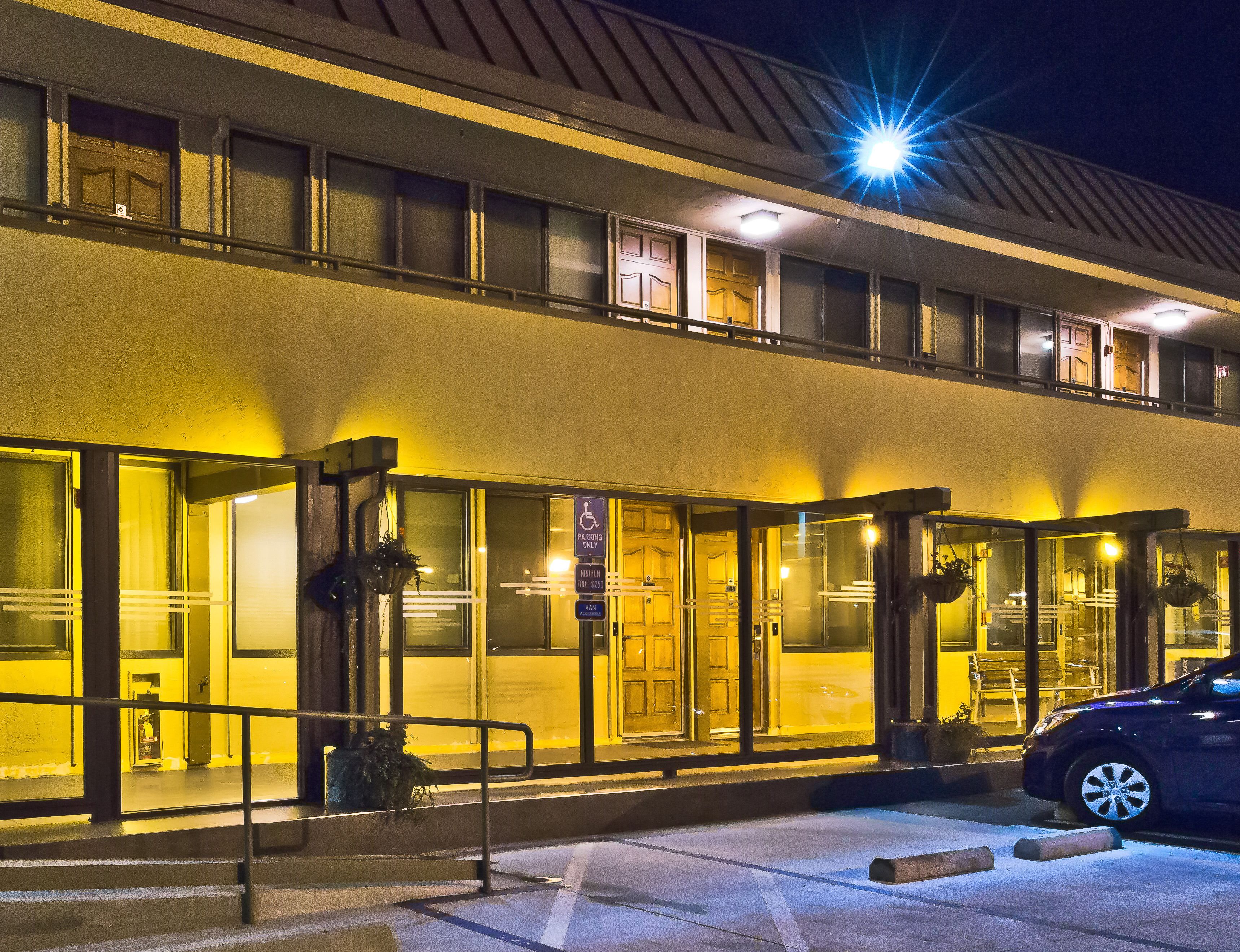 A hotel with a two-story structure, large windows, and a parking lot with a car.