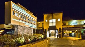 Entrada de hotel con un cartel que dice "HOTEL STRATA" y un camino pavimentado que conduce a la entrada.