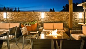 An outdoor patio with stone walls, cushioned seating, a glass-top table, and a fire feature. - Hotel Strata (Mountain View)