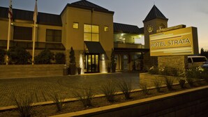 Een hotelentree met een bord waarop 'HOTEL STRATA' staat, een modern gebouw met een plat dak en een klokkentoren.