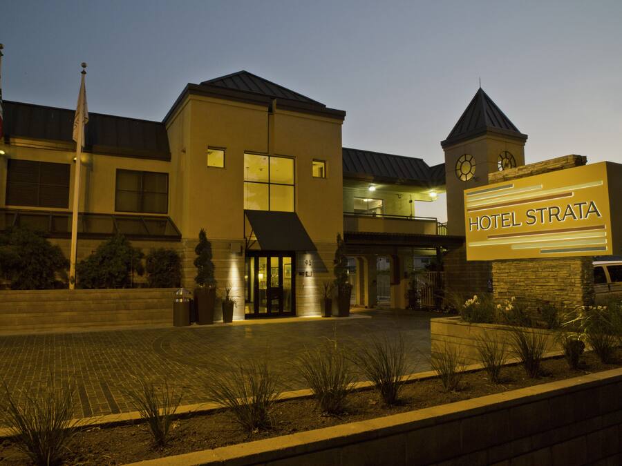 Entrada de un hotel con un letrero que dice "HOTEL STRATA", un edificio moderno de techos planos y una torre del reloj.