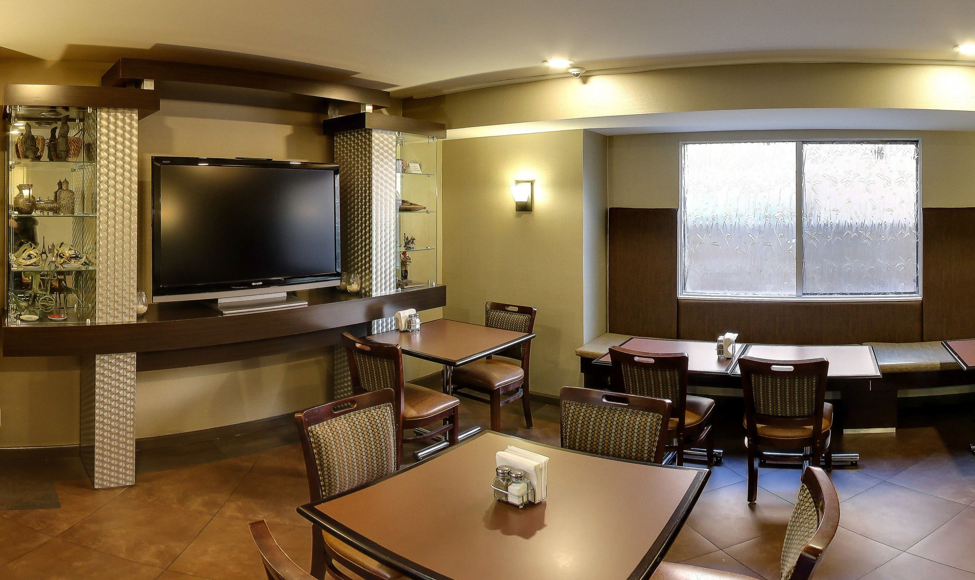 A restaurant with a flat-screen TV, multiple tables and chairs, and a large window with frosted glass.