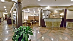 Een hotellobby met een receptiebalie, een zithoek en een trap.