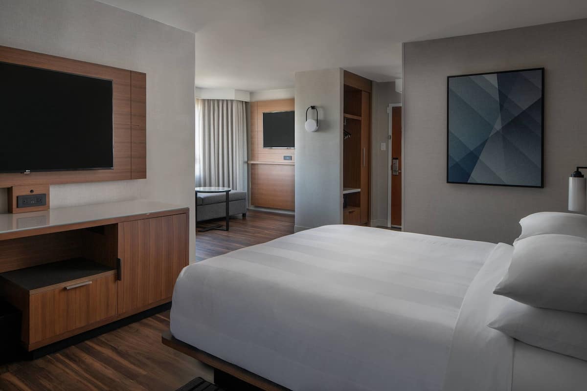 A hotel room with a large bed, a flat-screen TV mounted on the wall, a desk with a chair, and a wardrobe.