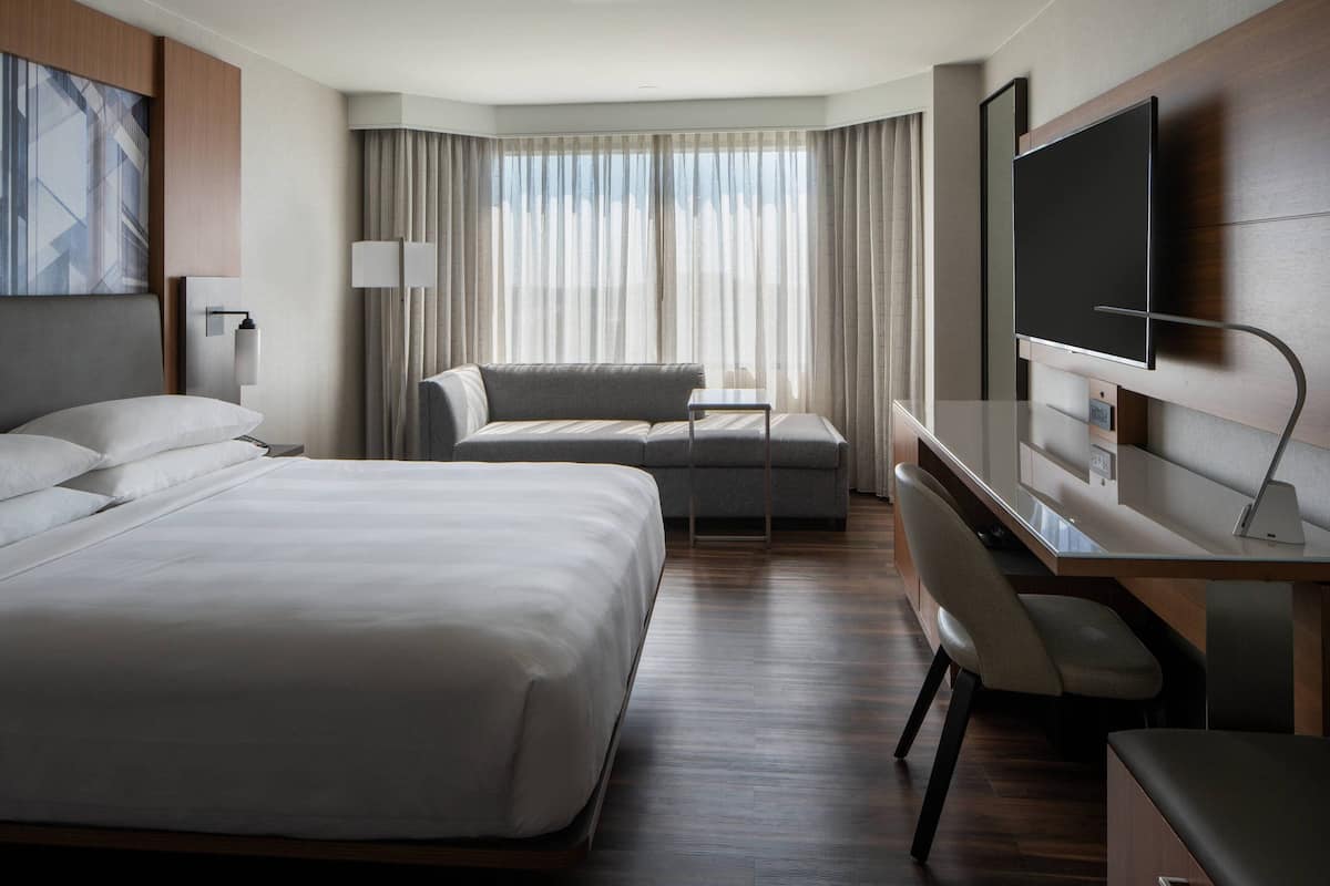 A modern hotel room with a large bed, a sofa, a desk, and a TV.