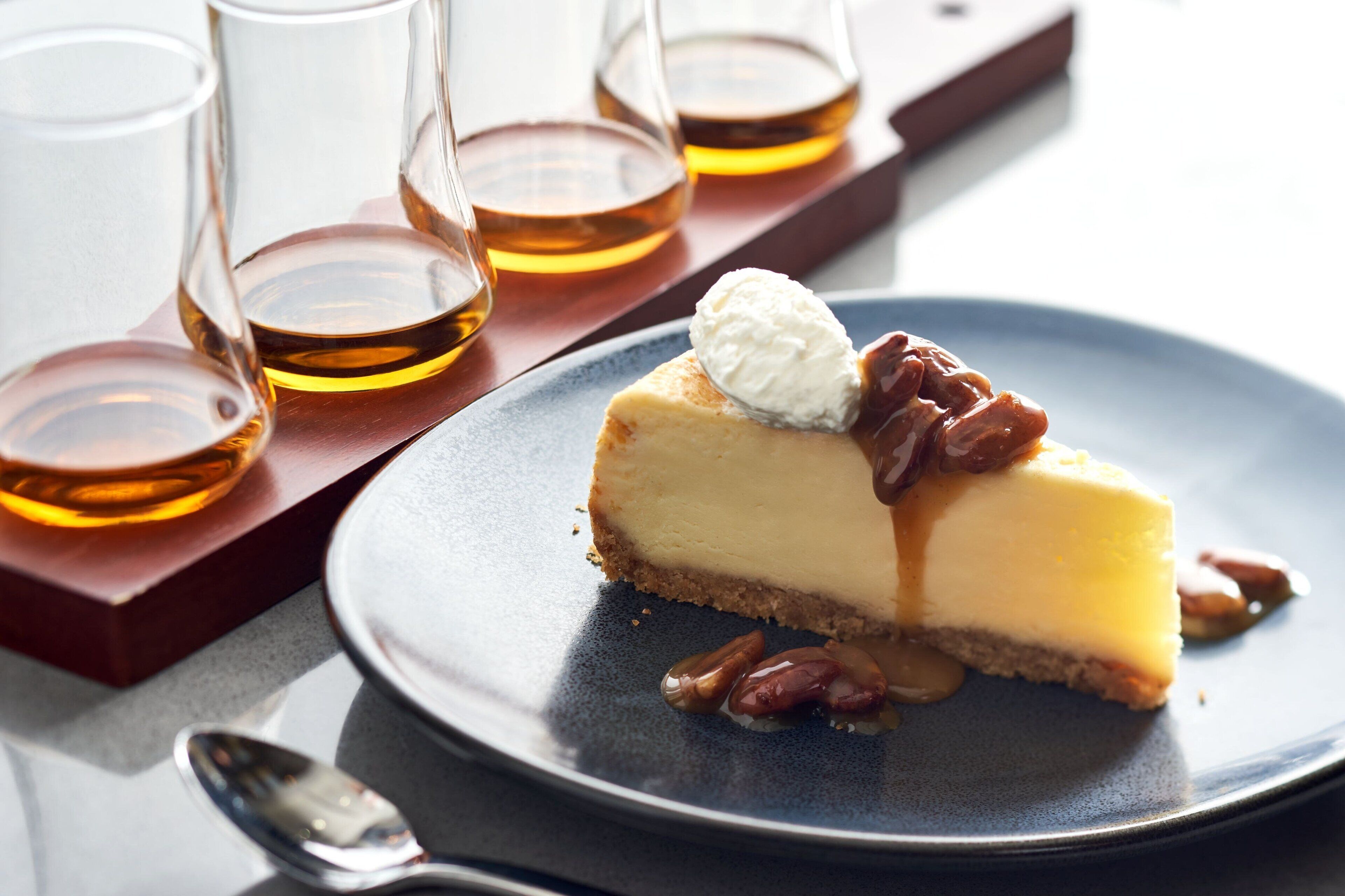 A slice of cheesecake with pecans and a scoop of ice cream on a plate, accompanied by three glasses of whiskey.