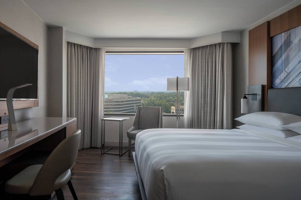A hotel room with a large bed, a desk, a chair, a small table, and a view of the outdoors.