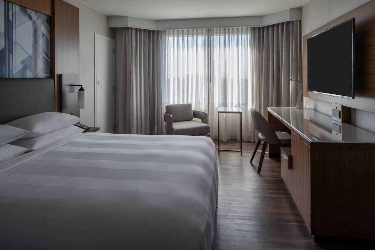 A hotel room with a large bed, a desk, a chair, a television, and a window with curtains.