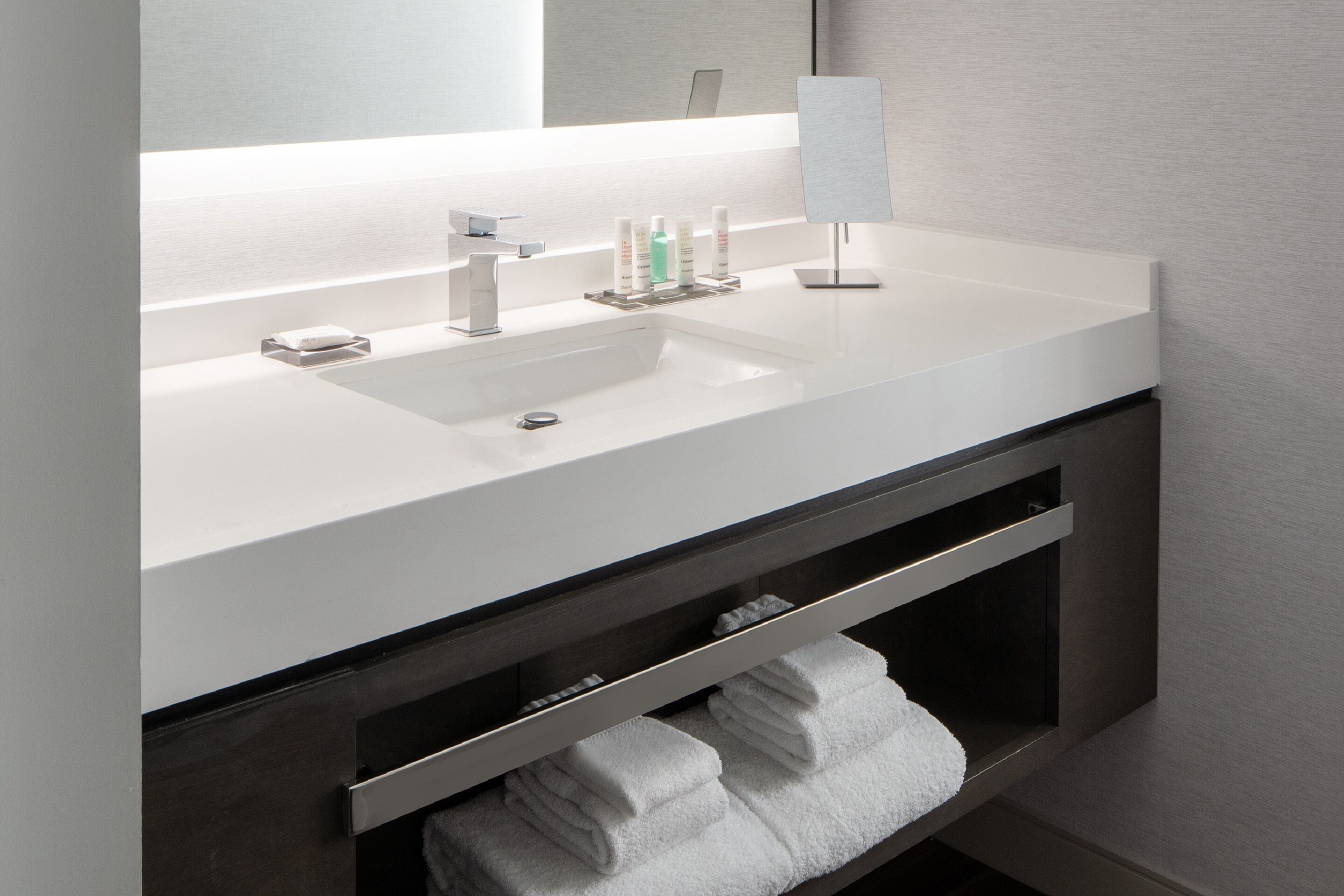 A modern bathroom with a white sink, mirror, and shelves for toiletries.